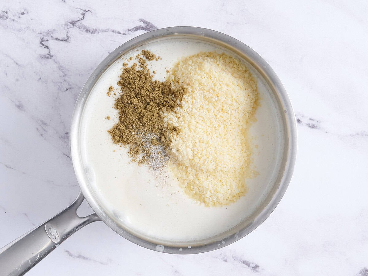 Seasonings and parmesan added to bechamel sauce in a saucepan.