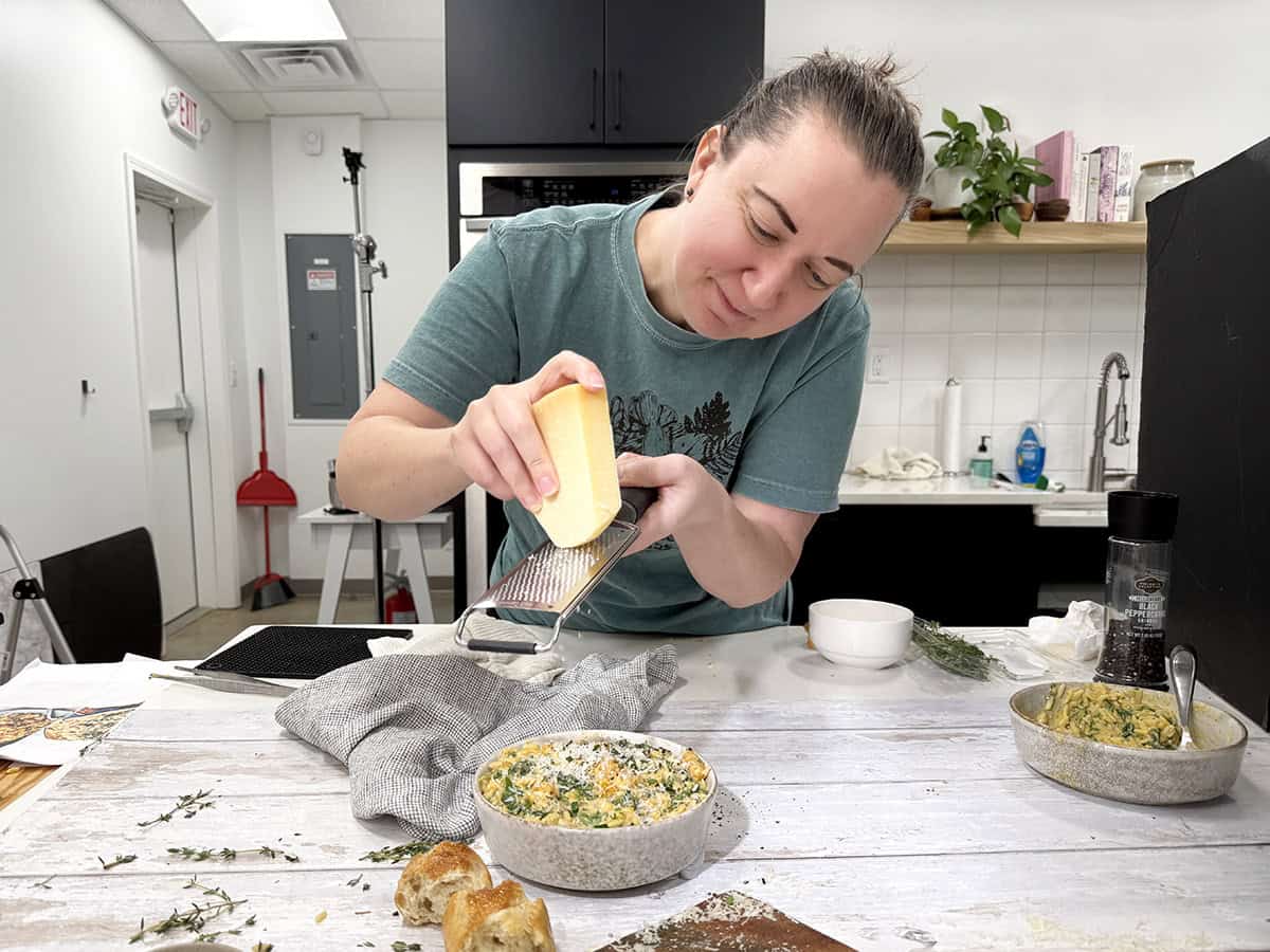 A woman shredding fresh parmesan over a bowl on butternut squash orzo in a kitchen.