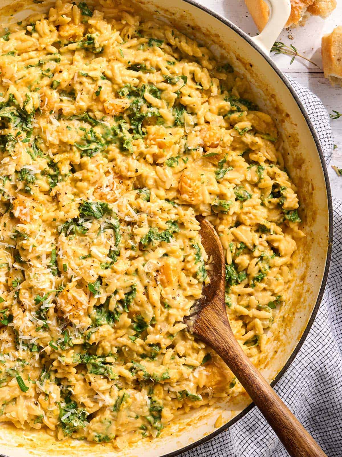 Overhead close up view of a skillet of creamy butternut squash orzo with a wooden spoon.