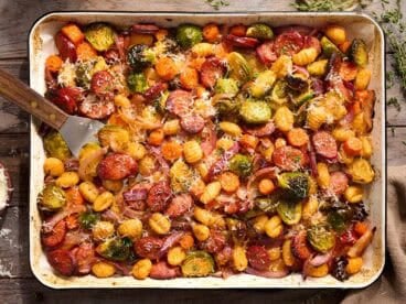 Overhead view of gnocchi with sausage and fall vegetables on a sheet pan.