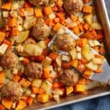 Overhead view of sheet pan turkey meatballs and root vegetables with a metal spatula.