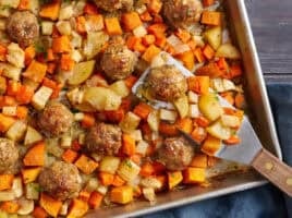 Overhead view of sheet pan turkey meatballs and root vegetables with a metal spatula.